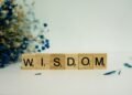 a wooden block spelling the word wisdom next to a bouquet of flowers